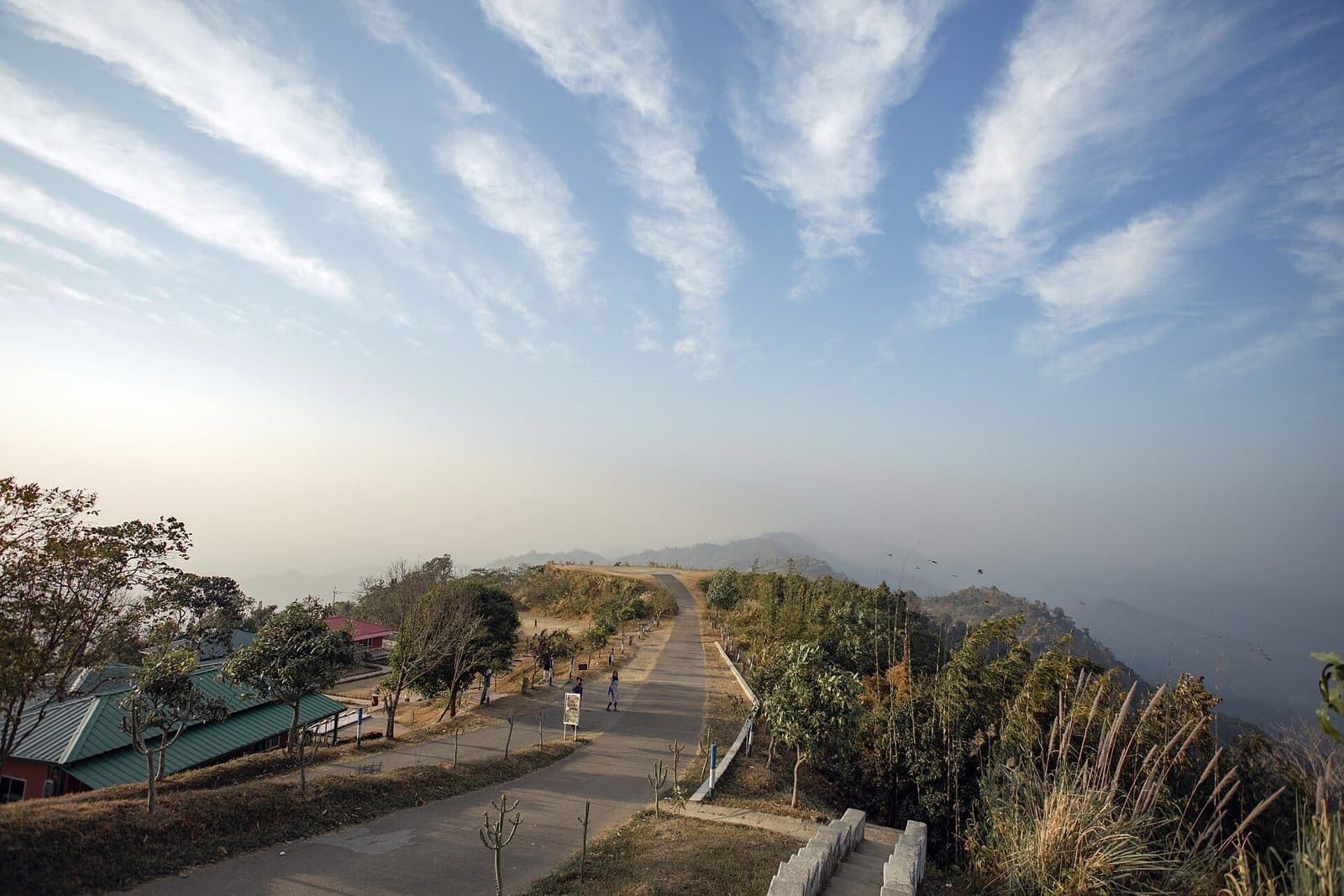 Road along the ridge at Nilgiri in Bandarban, with forested hills fading into haze under a streaked sky
