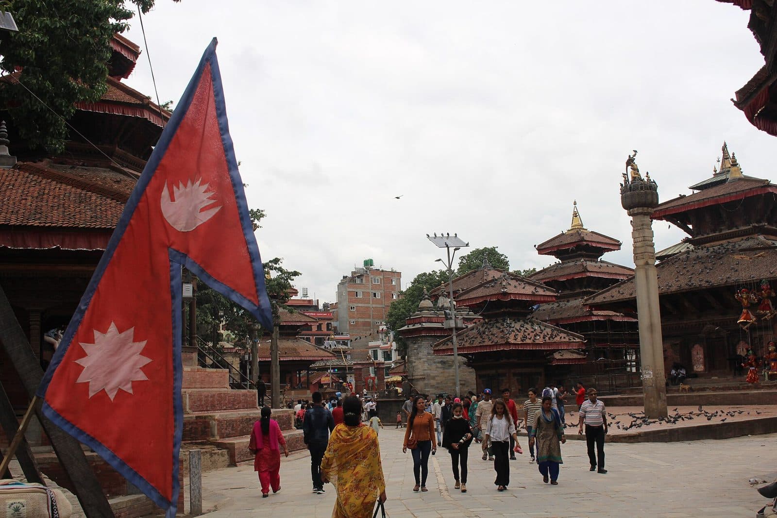 Nepali flag in the foreground with pagoda temples and visitors in Kathmandu Durbar Square