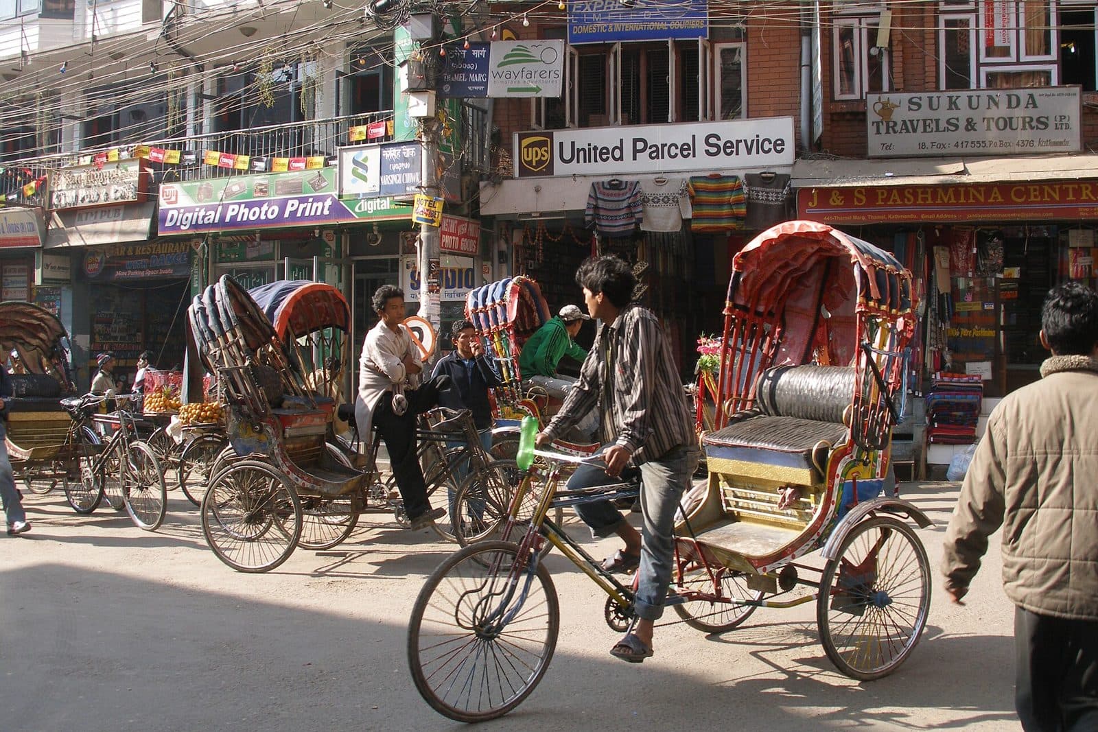 Cycle rickshaws and pedestrians on a busy street lined with shop signs in Thamel, Kathmandu